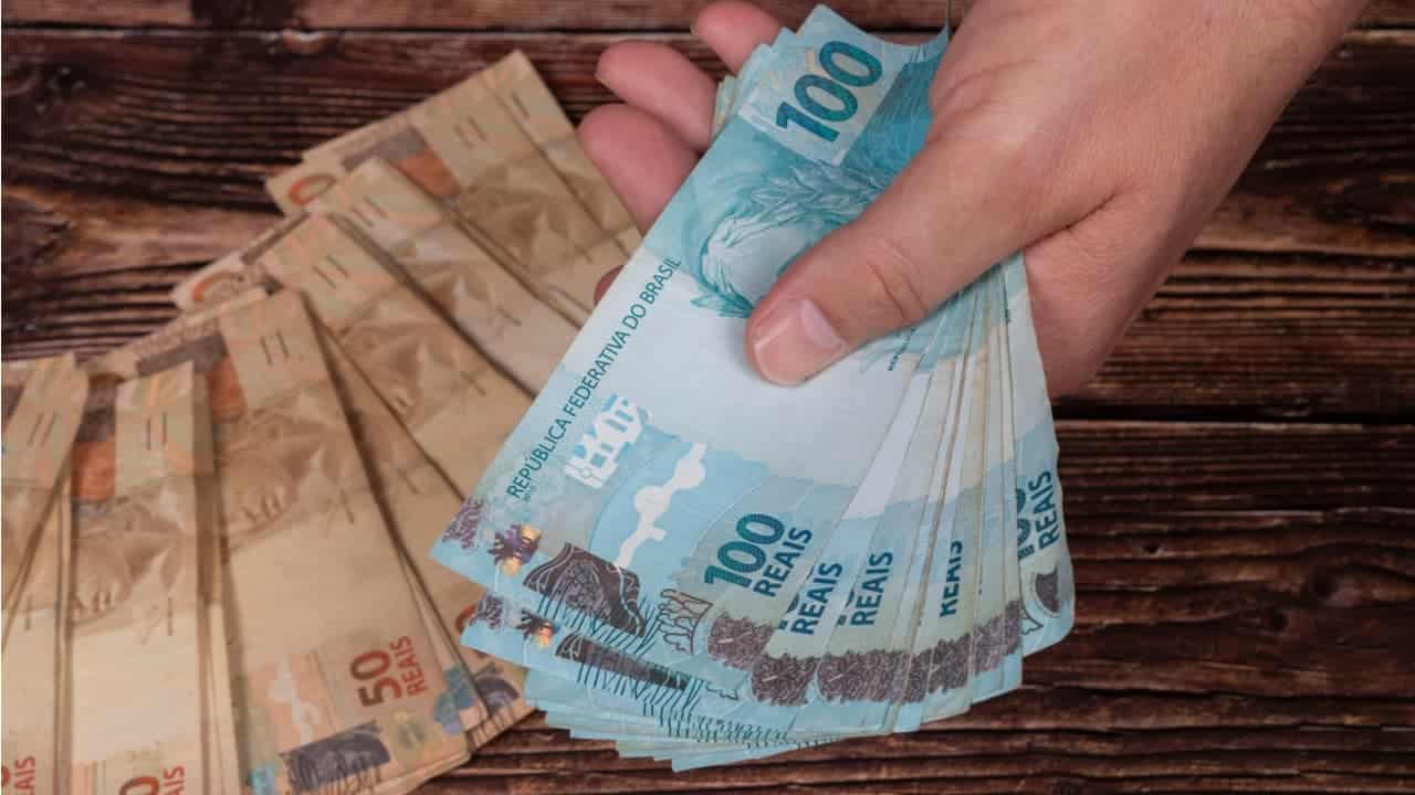Imagem de várias notas de 100 e 50 reais na mão de uma pessoa