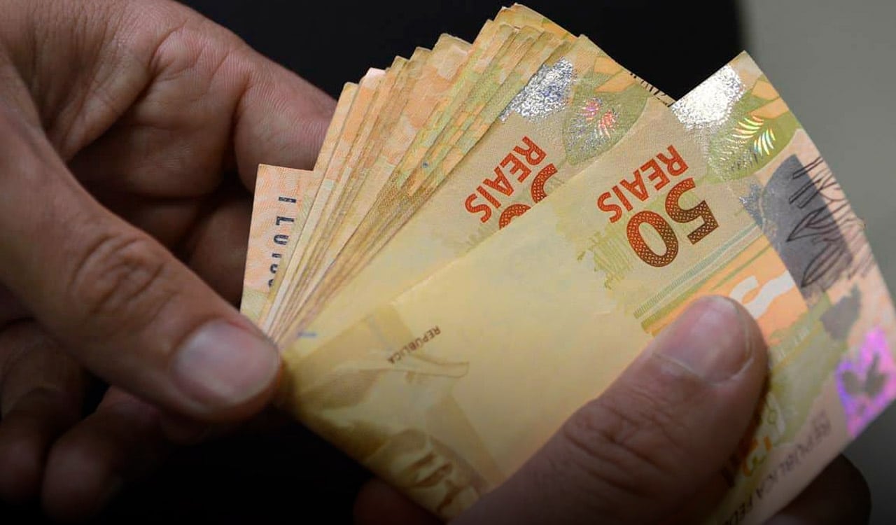 Mão segurando várias notas de cinquenta reais