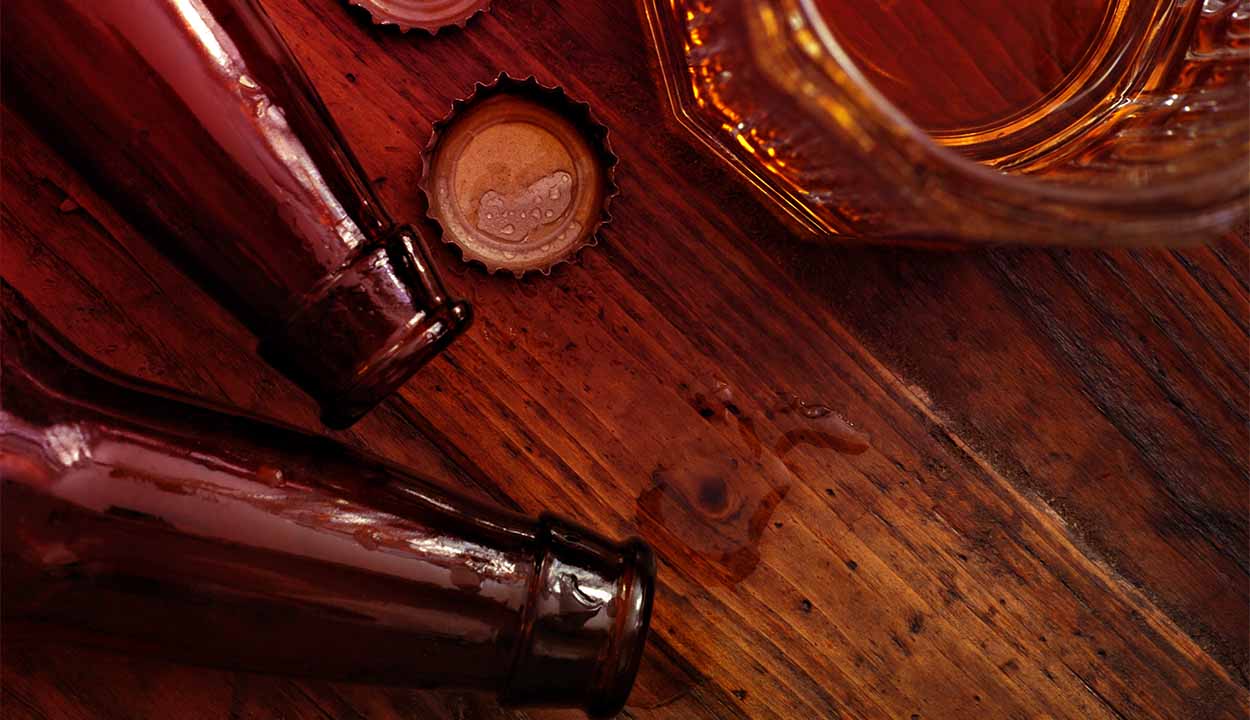 Closeup na imagem de garrafas de cerveja caidas em uma mesa, tampas e um copo