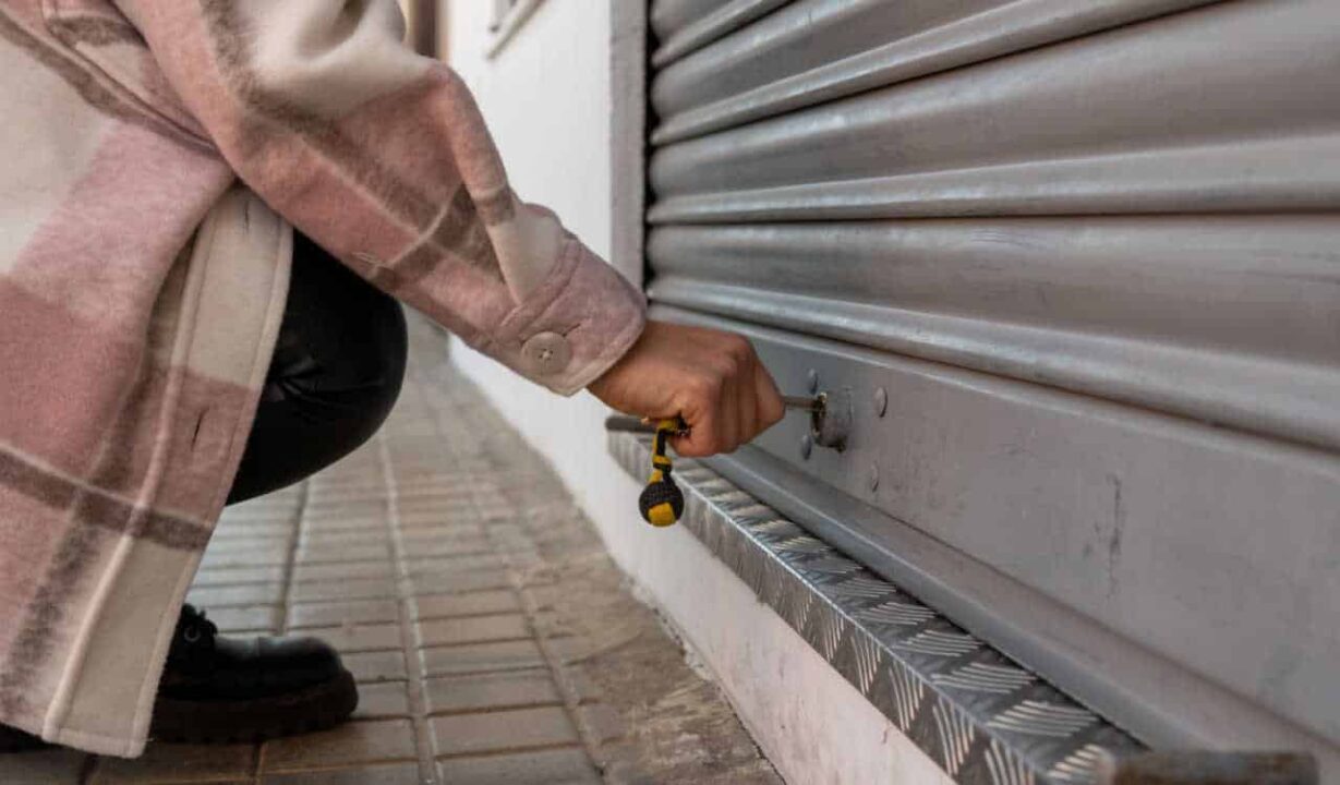 Pessoa fechando uma porta de metal de um estabelecimento comercial