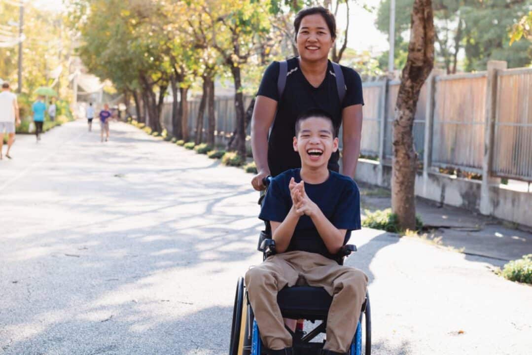 mãe com expressao feliz auxiliando o filho cadeirante