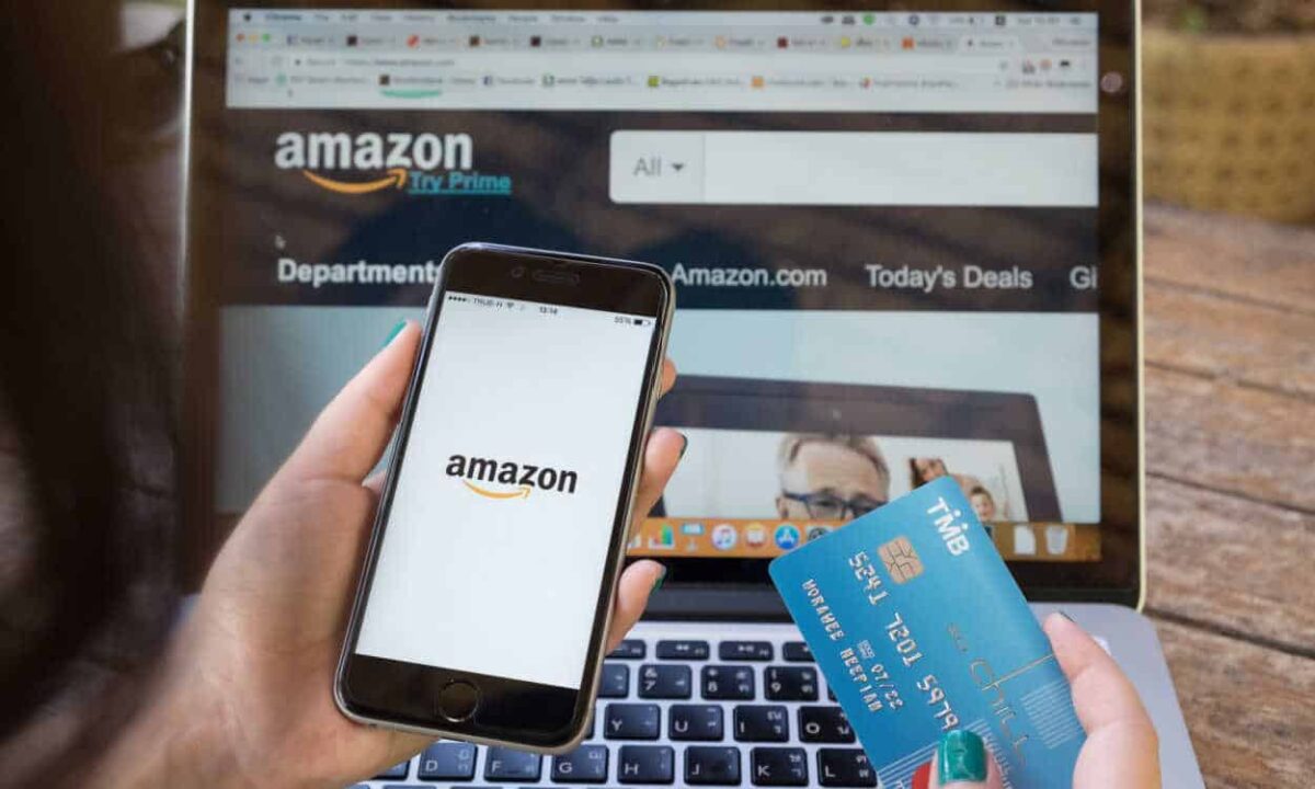 Pessoa segurando um celular com a logo da Amazon em uma mão e na outra um cartão de crédito.
