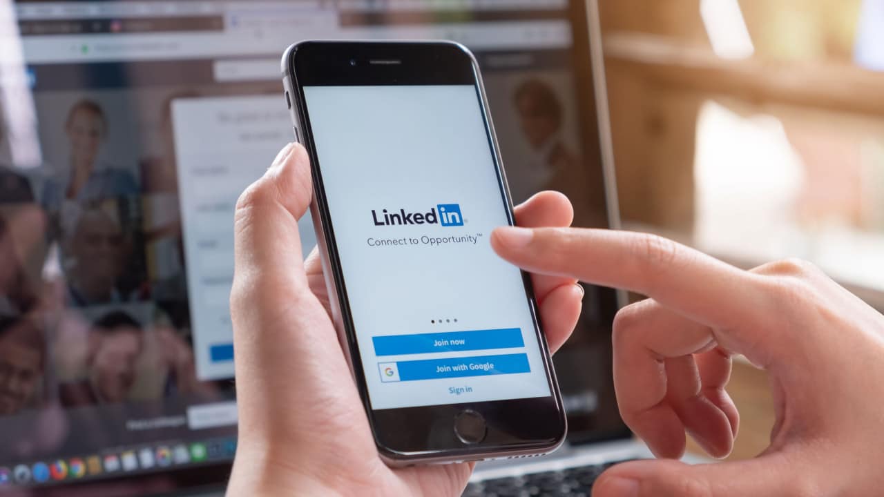 Mão segurando o celular ligado na interface do LinkedIn, plataforma que demitiu funcionários.