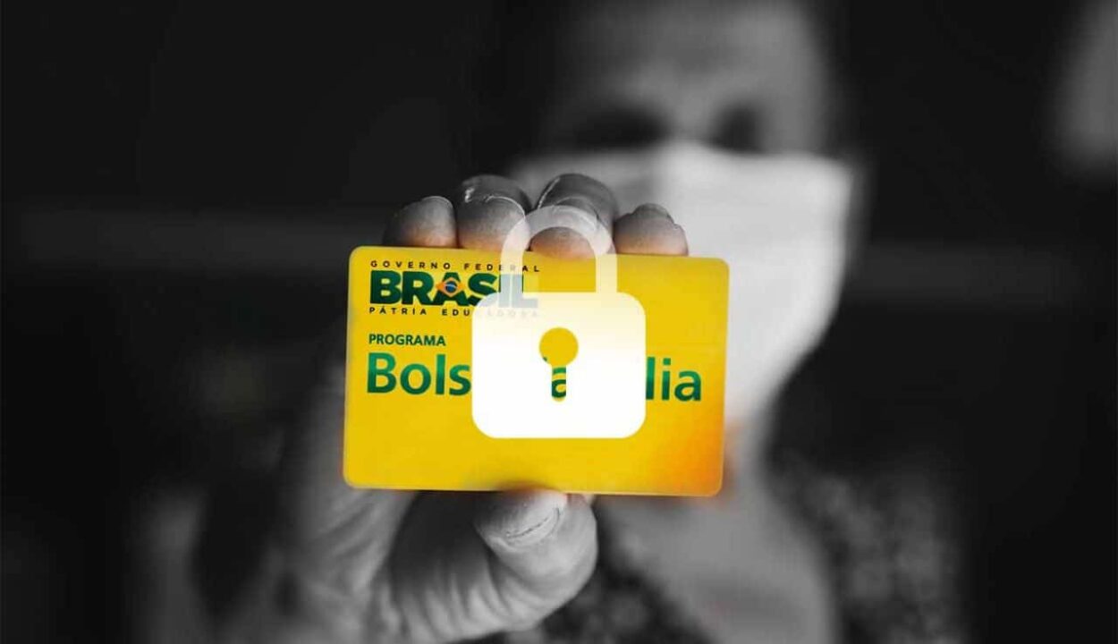 Pessoa com máscara no rosto e segurando um cartão do Bolsa Família com a ilustração de um cadeado em cima, indicando bloqueio.