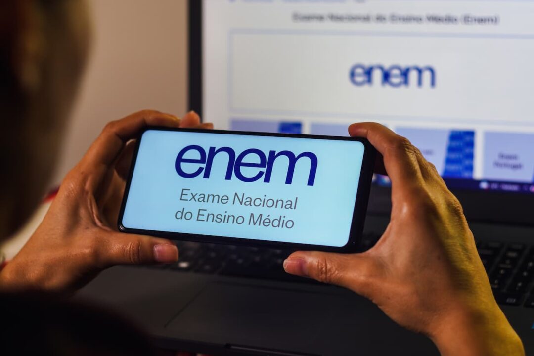 Pessoa segurando celular exibindo página do Enem, o Exame Nacional do Ensino Médio.