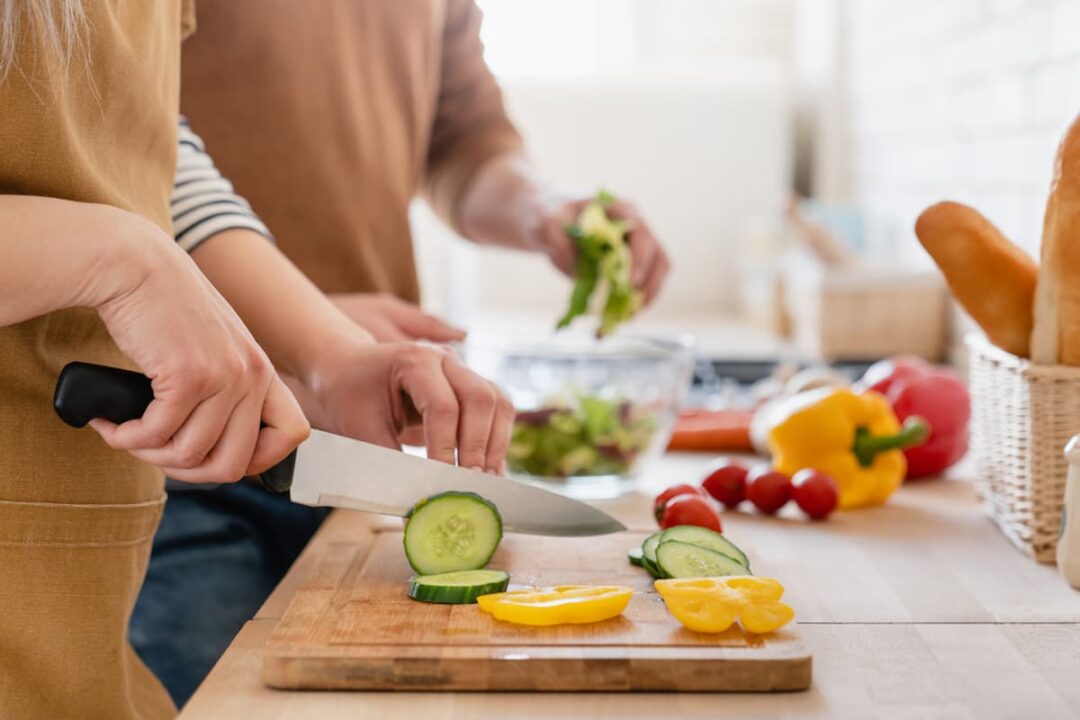 Imagem de pessoas cortando alimentos na cozinha