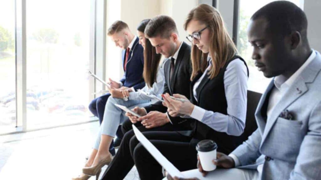 Entrevistas de emprego estão sendo reformuladas e novo modelo pode frustrar candidatos; entenda 1 Profissionais sentados aguardando entrevista de emprego em uma fileira. exame