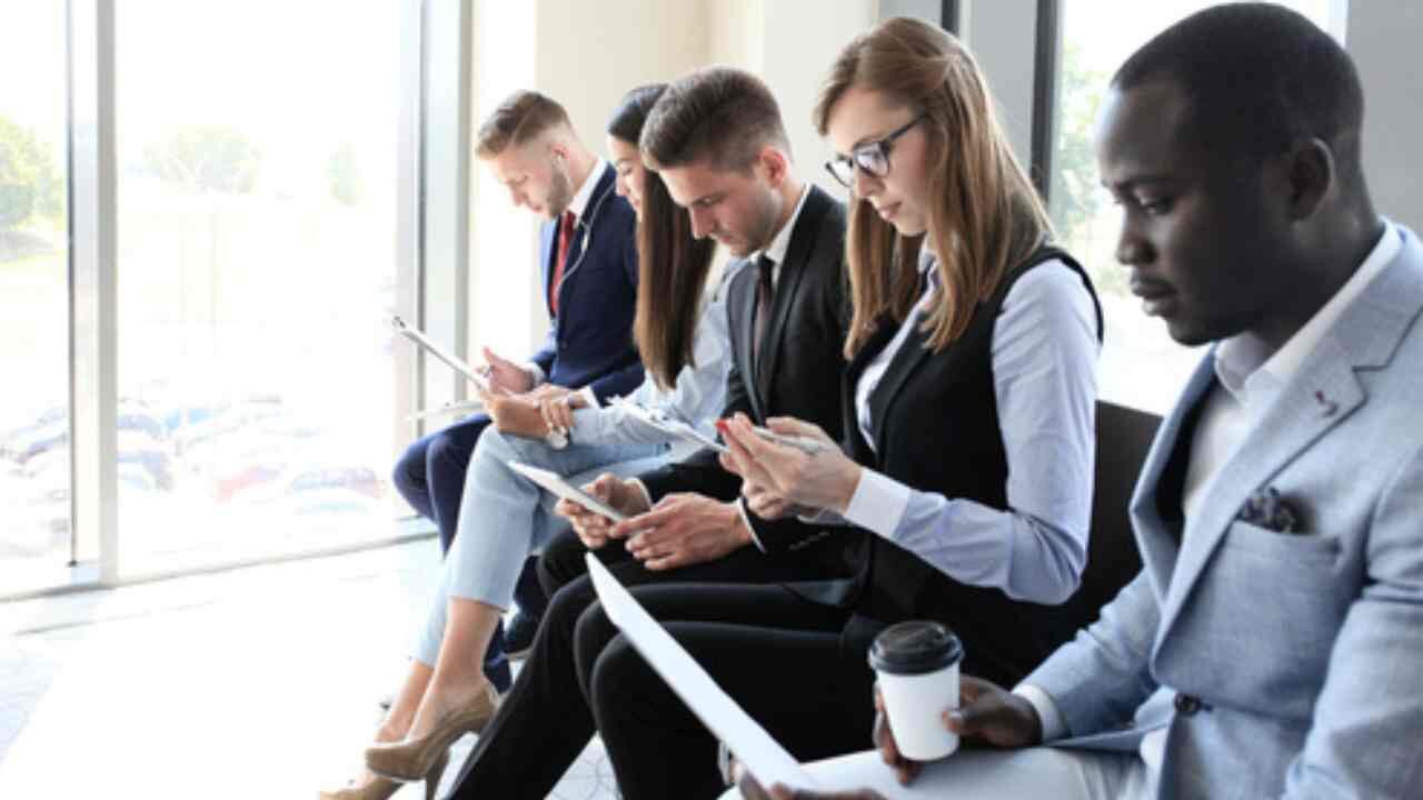 Profissionais sentados aguardando entrevista de emprego em uma fileira. exame