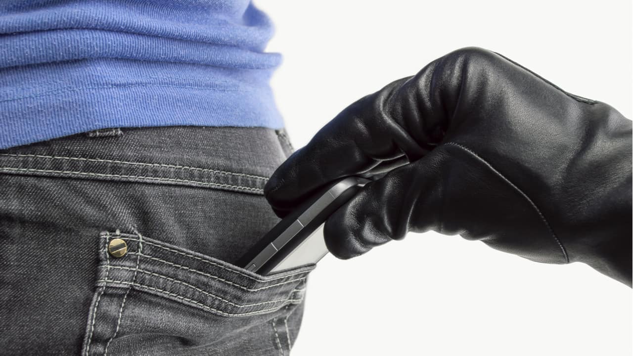 A imagem mostra um Celular no bolso traseiro e uma mão, com luva preta, retirando o aparelho.
