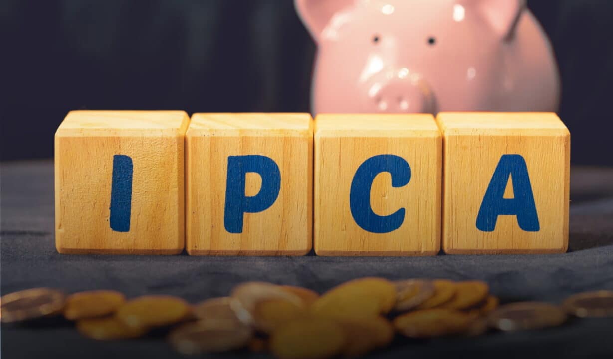 Imagem mostra bloquinhos com as letras IPCA. Atrás, está um cofre em formato de porquinho rosa e, na frente, algumas moedas espalhadas.
