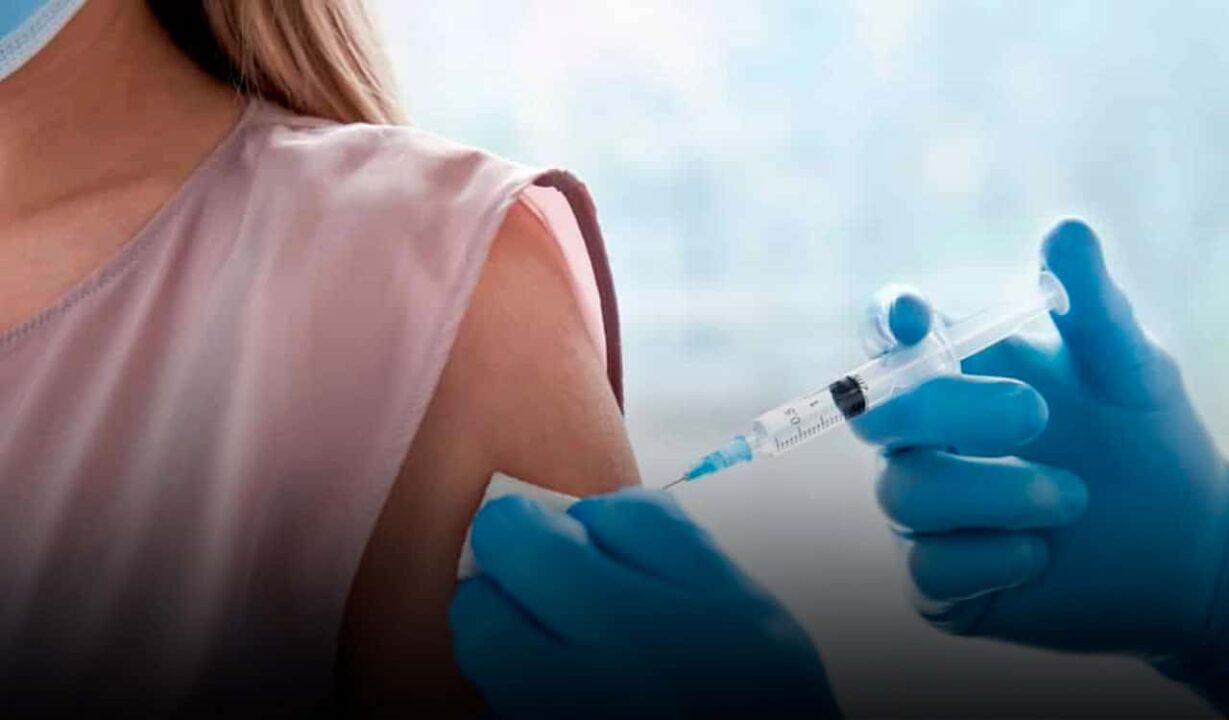 beneficiária do Bolsa Família recebendo vacina no braço, aplicada por profissional da saúde