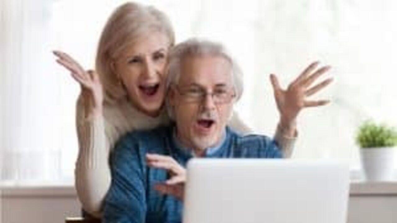 Casal de idosos comemorando em frente a um notebook