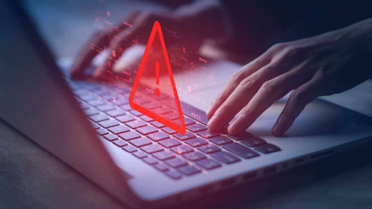 mãos no teclado do laptop e um alerta na cor vermelha, alertando algum perigo na rede