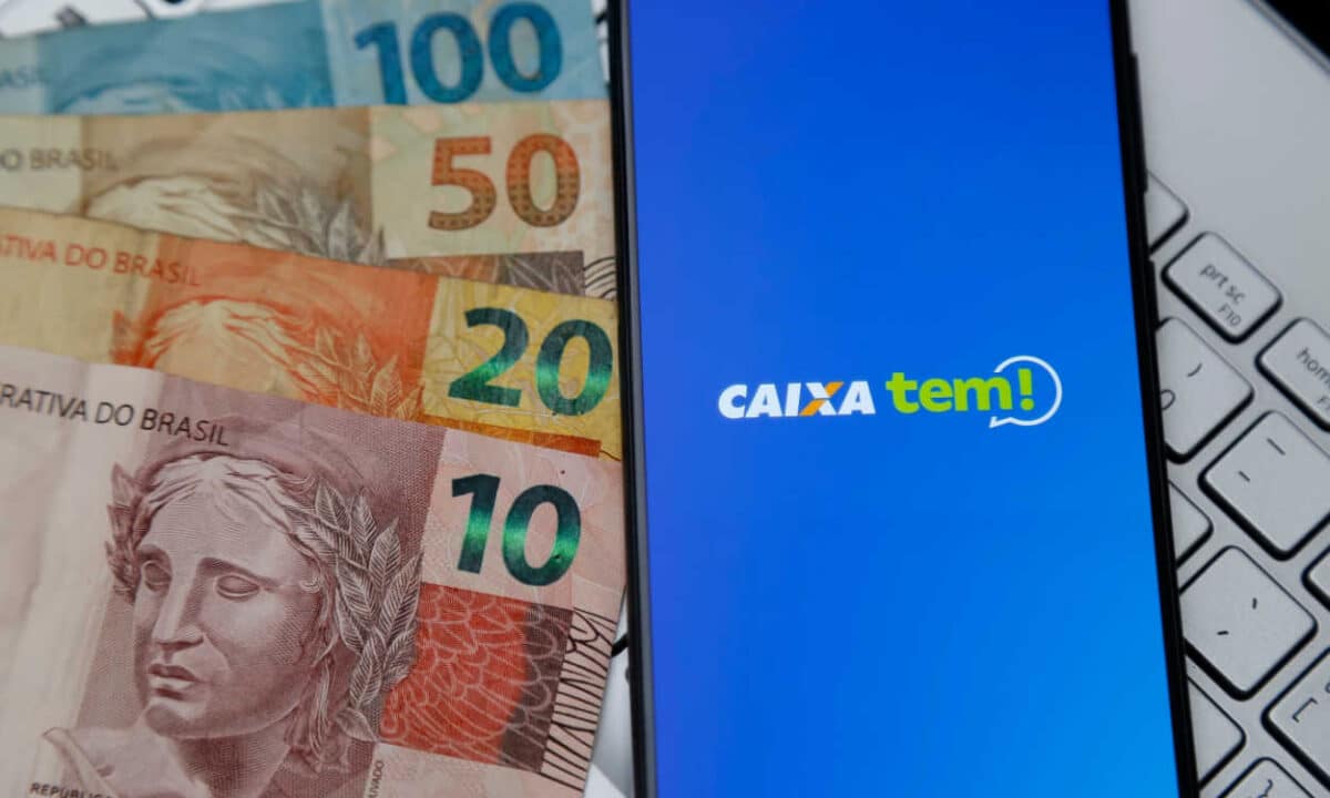 Celular com a logo do Caixa Tem na tela ao lado de várias notas de dinheiro