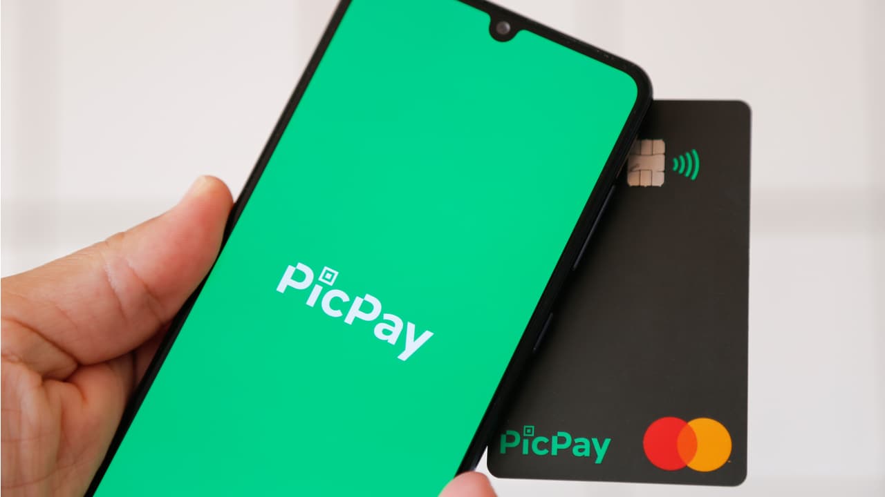 Cartão do PicPay e aplicativo do PicPay aberto no celular, ambos segurados por uma mão.