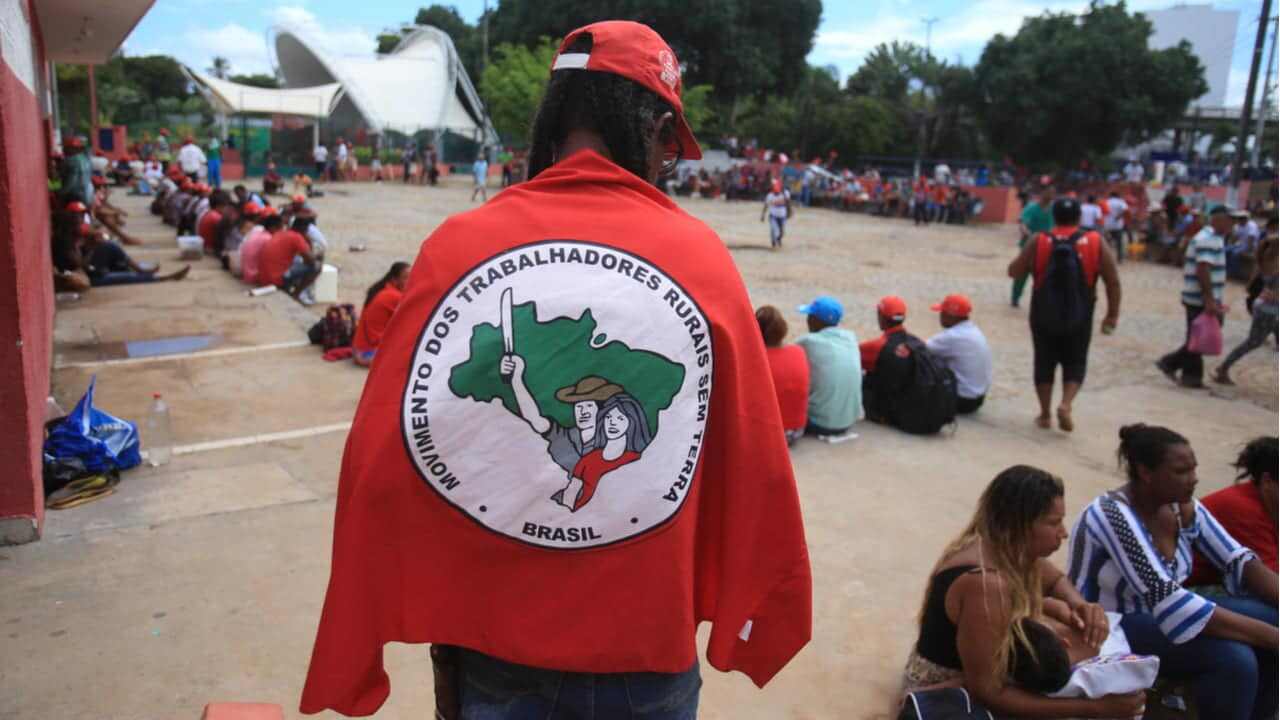 Homem de costas coberto com bandeira do MST (Movimento dos Trabalhadores Rurais Sem Terra)
