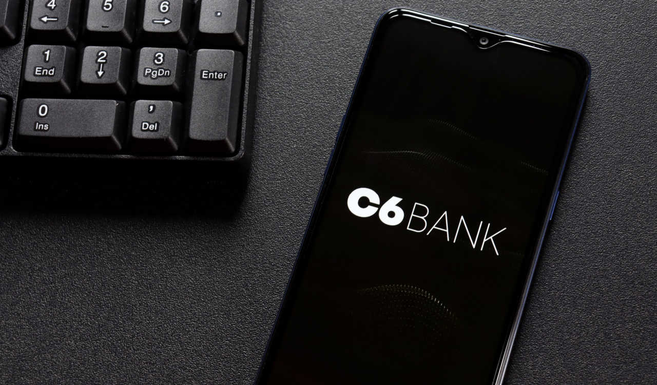 Celular com a logo do C6 Bank na tela ao lado de um teclado numérico