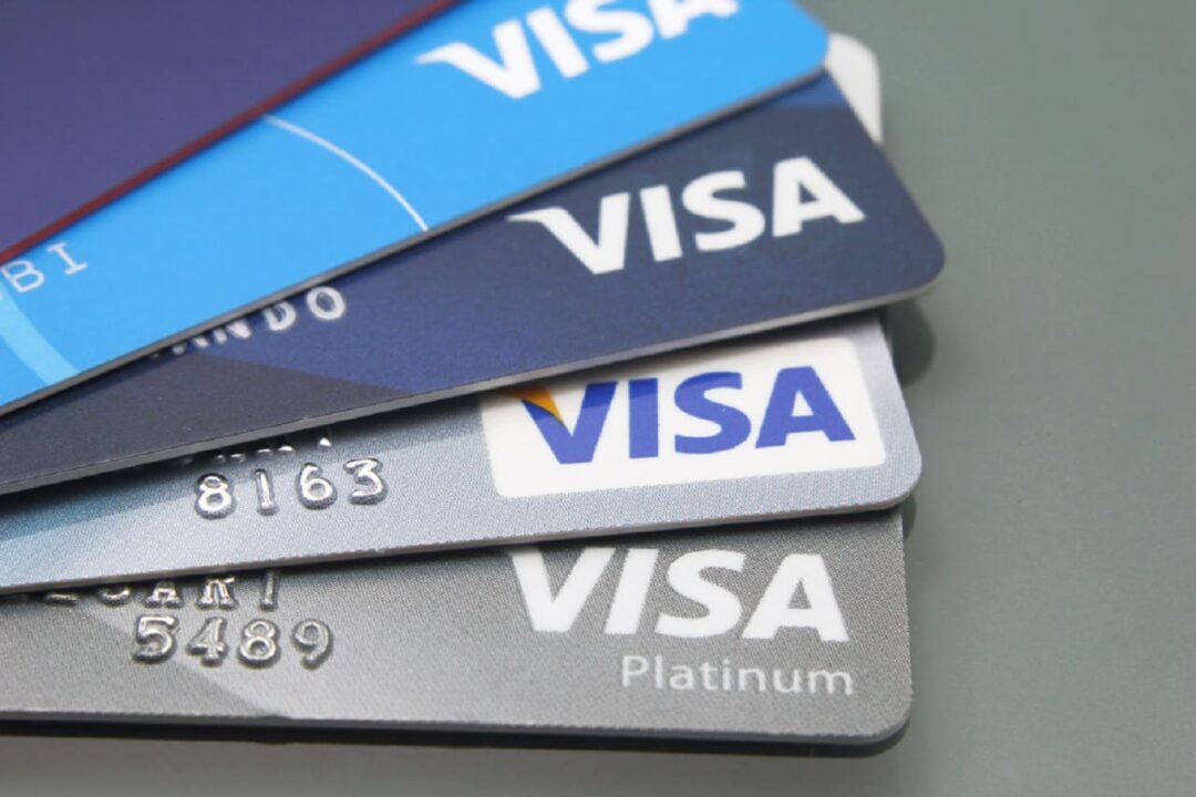Cinco unidades de cartão de crédito Visa empilhados em forma de leque sobre uma superfície cinza.