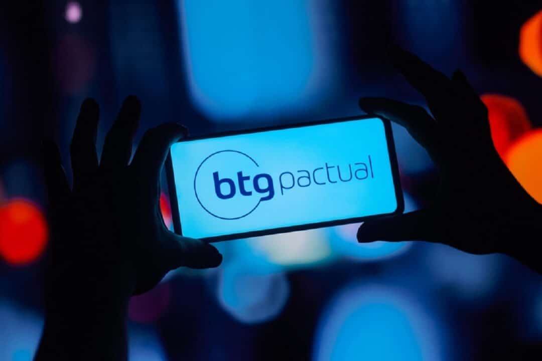 Imagem de duas mãos segurando um celular com a logo do BTG Pactual