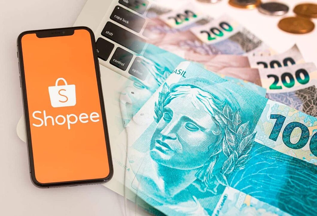 celular com aplicativo da Shopee ao lado de notas de 100 e 200 reais
