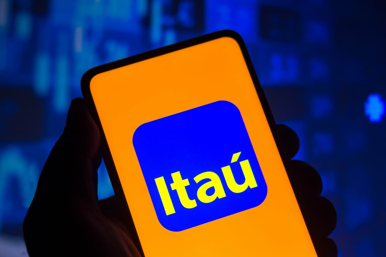 maõ segurando celular com o logo do banco Itaú em um fundo azul