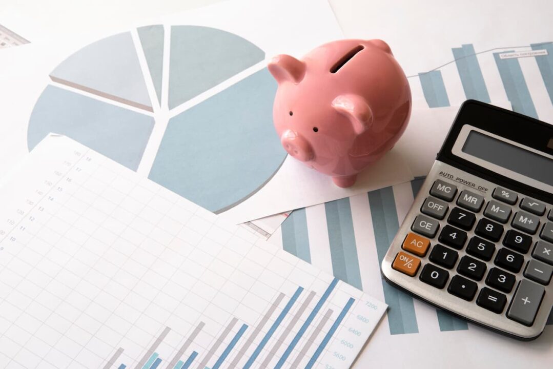 Um cofrinho de porco pequeno e uma calculadora em cima de papeis. A imagem tem um teor financeiro. crescimento da economia no Brasil em 2024