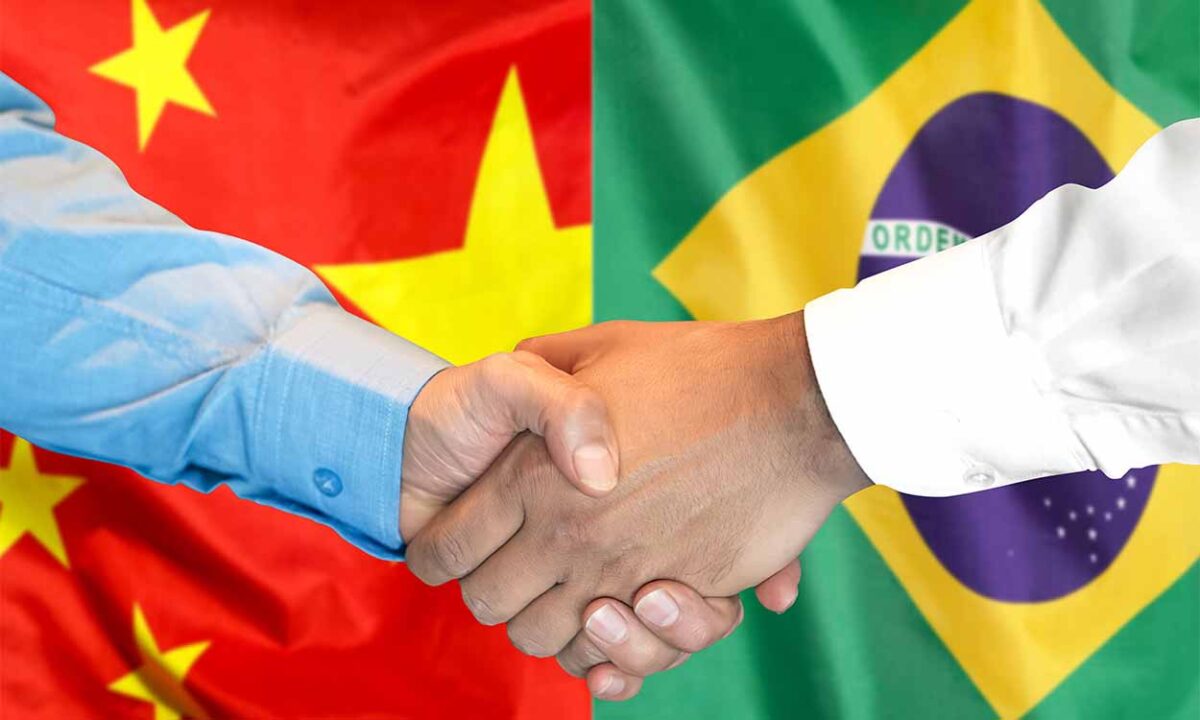 Duas pessoas dando as mões com as bandeiras da China e do Brasil ao fundo