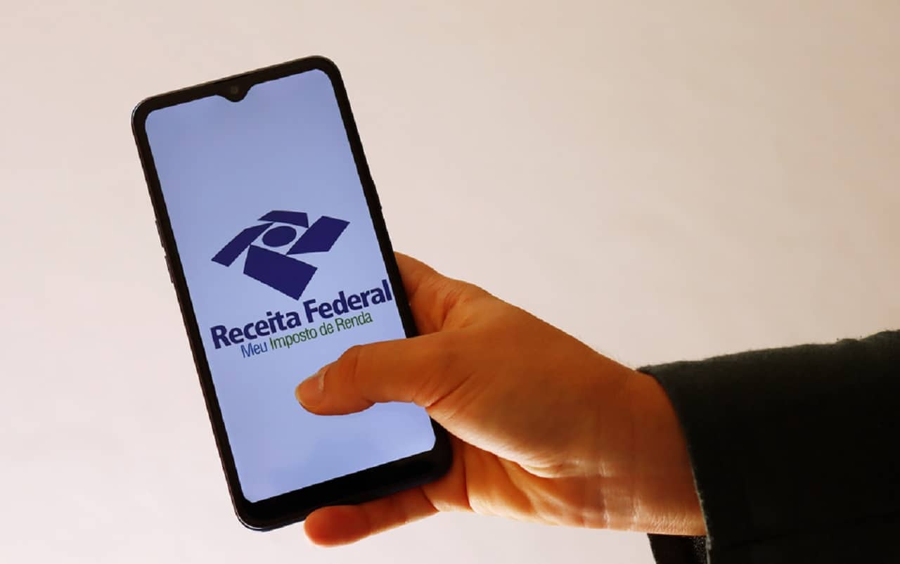 Imagem de uma mão mexendo em um celular com a logo da Receita Federal