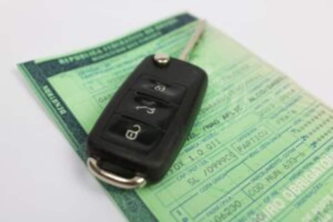 Chave de carro em cima da CNH dispostos sobre uma superfície lisa e branca