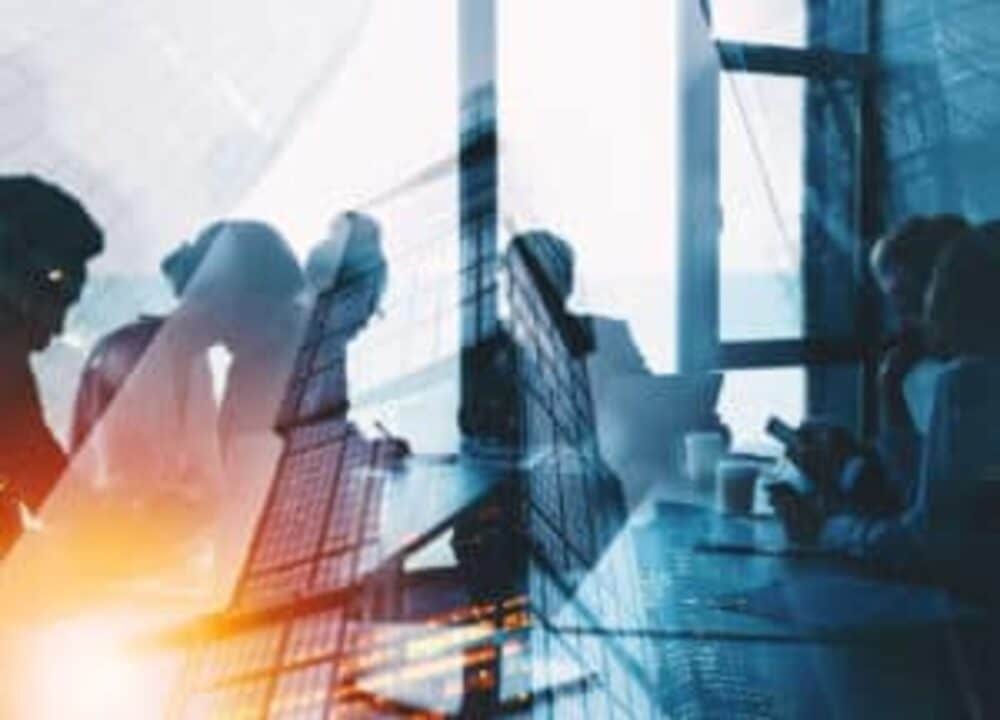 Pessoas trabalhando diante de uma luz azul e amarela com uma prédio comercial no meio remetendo às empresas