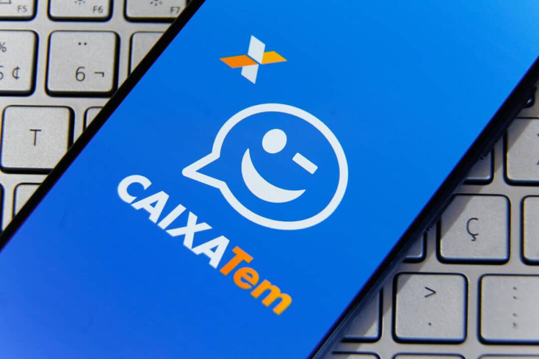 Celular com a tela inicial do aplicativo Caixa Tem, sobre um teclado de notebook.
