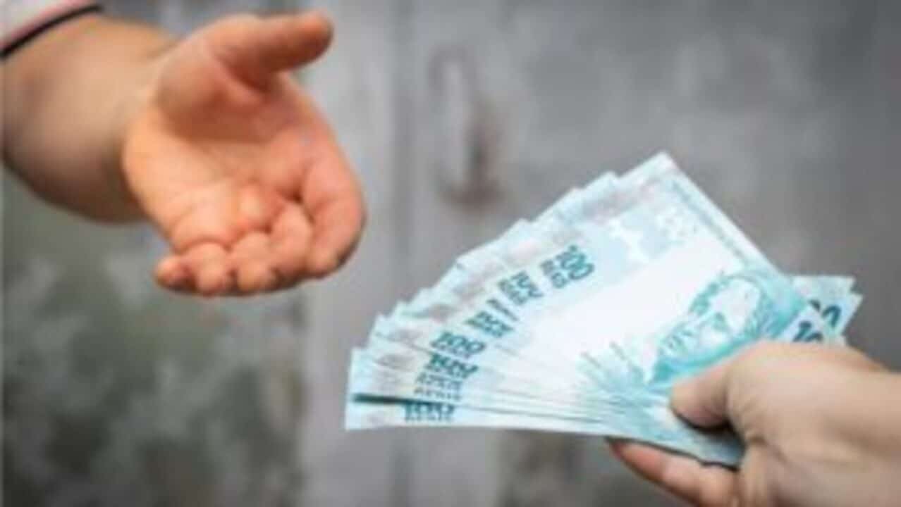 Pessoa com a mão esticada em direção de notas de 100 reais, ilustrando o conceito de empréstimo consignado