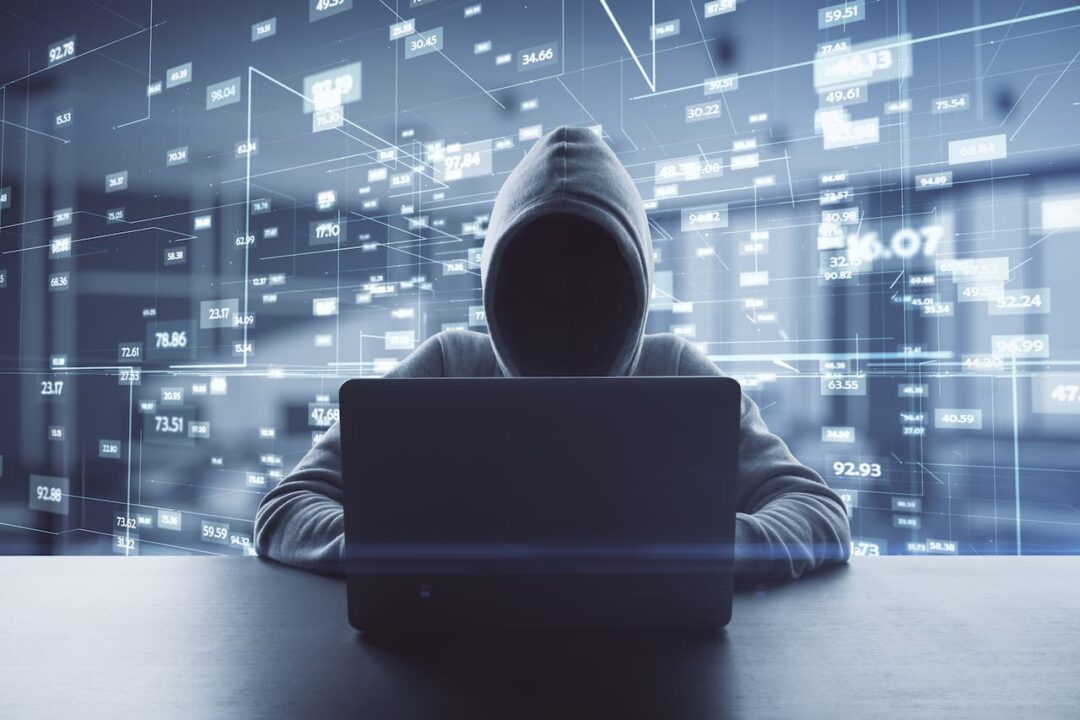 hacker encapuzado usando notebook, ao fundo tem vários códigos ciberneticos
