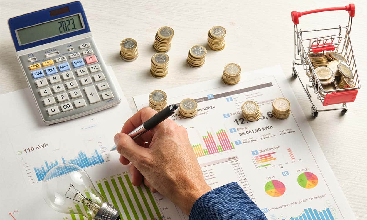 Mão masculina fazendo contas em papéis rodeados de moedas e uma calculadora
