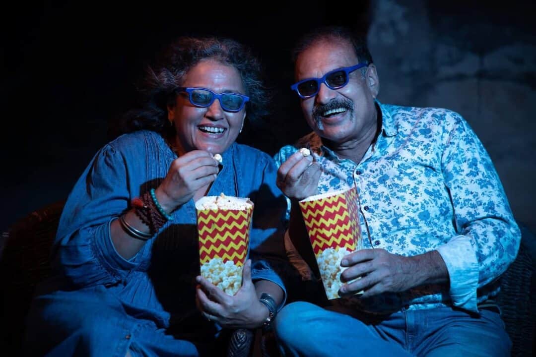 Dois idosos sentados em uma sala de cinema e comendo pipoca.