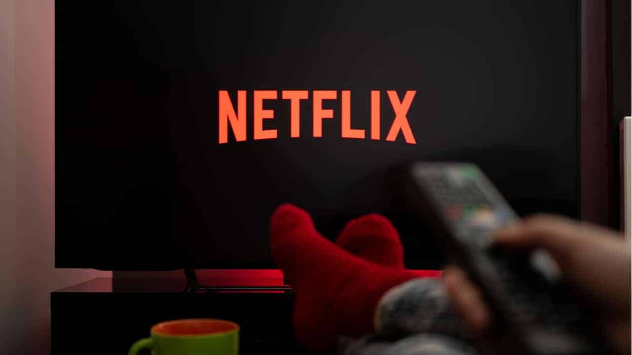 Imagem de pessoa com os pés apoiados em uma mesa de centro enquanto assiste à plataforma Netflix