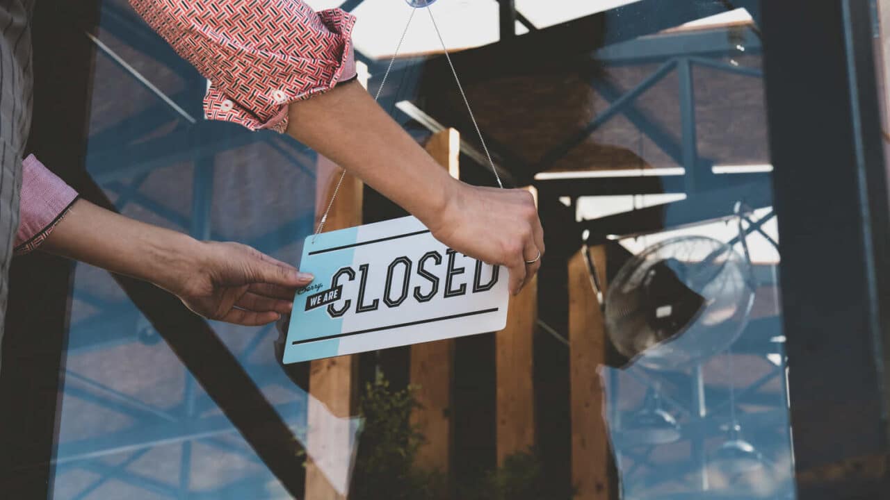 Pessoa colocando uma placa escrito "closed" na porta de um estabelecimento