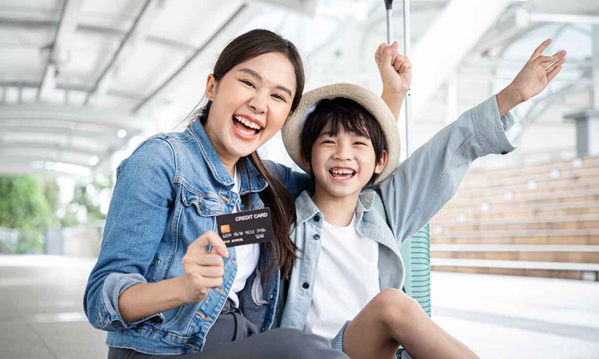 Duas pessoas comemorando com um cartão de crédito a mão. Elas parecem mãe e filho