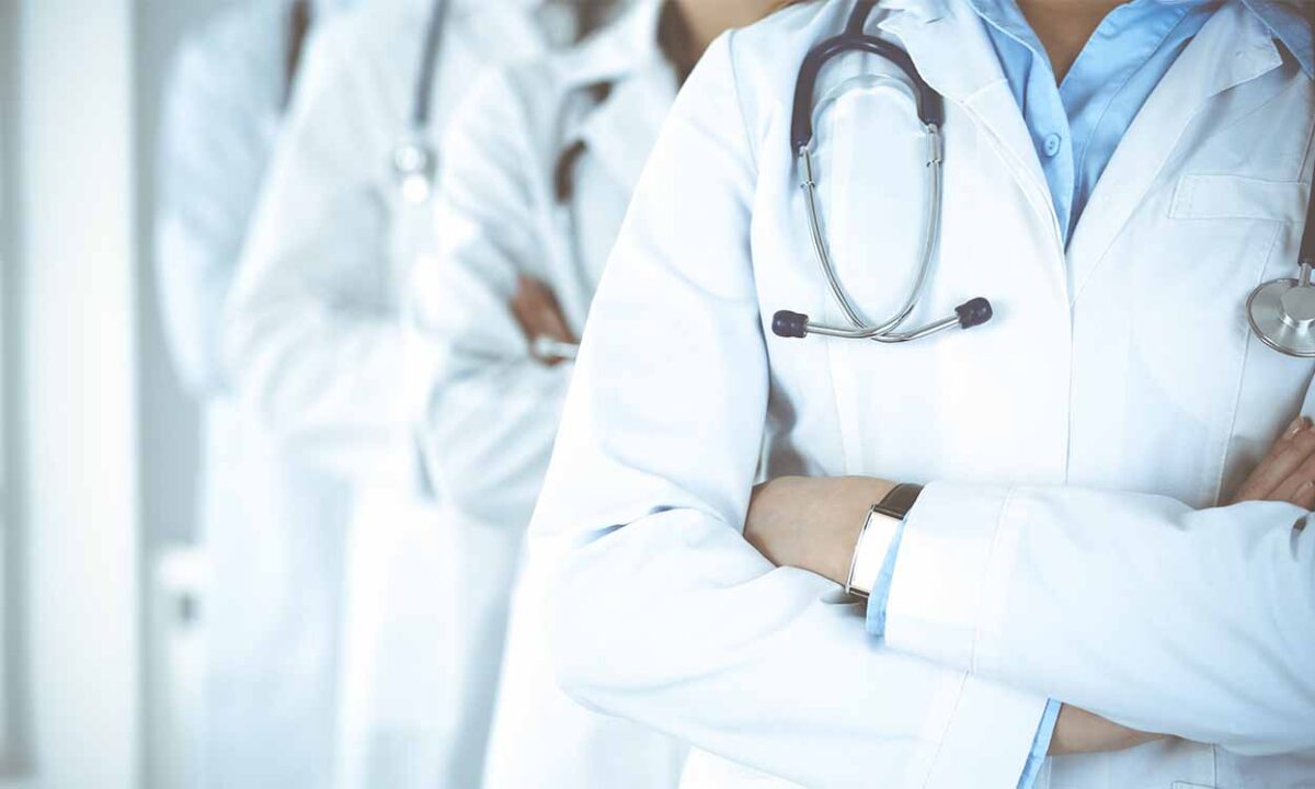 Médicos de braços cruzados utilizando jalecos brancos. Os pescoços estão cortados da imagem