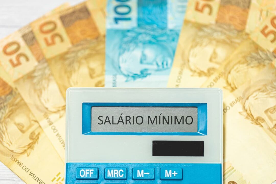 Leque com notas de 50 e 100 reais e uma calculadora com A tela anunciando "Salário Mínimo".