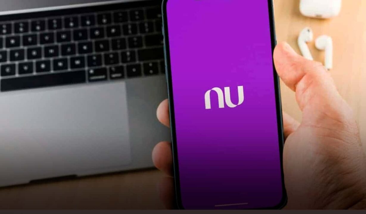 Mão segurando celular que exibe tela com app Nubank aberto.