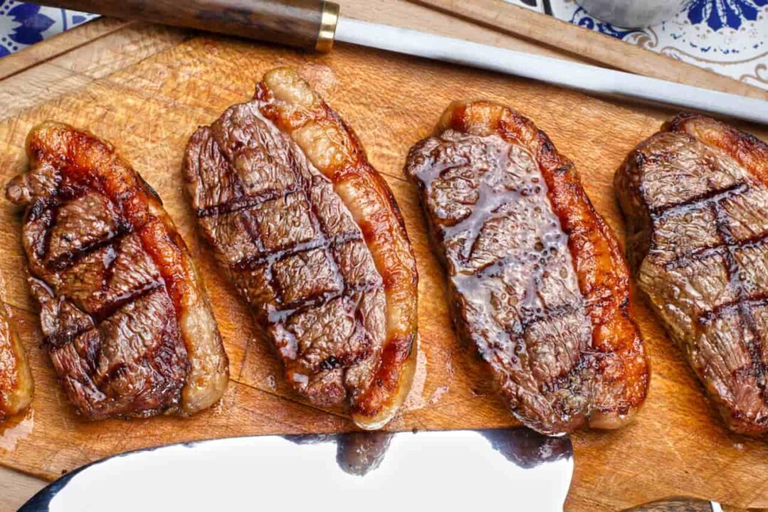 Quatro pedaços de picanha grelhada sobrepostos em uma tábua de carne, representando a queda do preço.