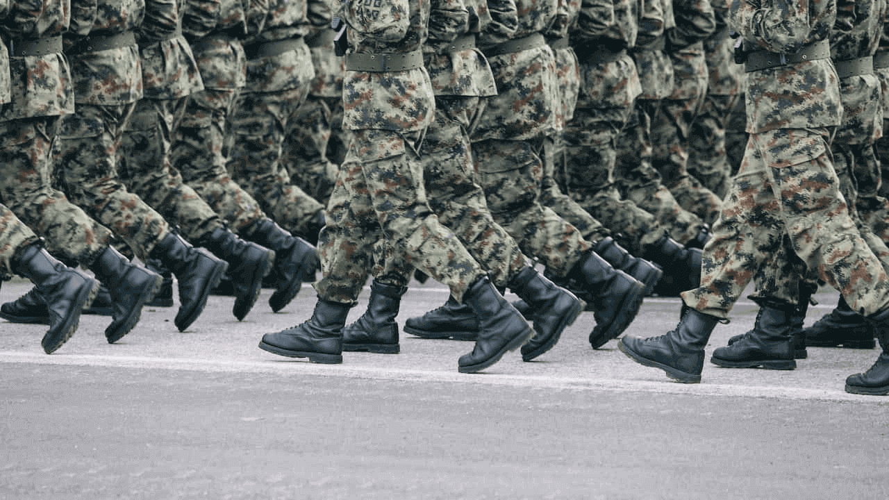 Soldados com roupas camufladas marchando de maneira sincronizada. A imagem os pega apenas até a altura do peito