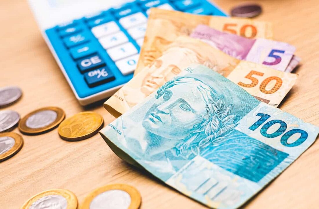 Notas de dinheiro, moedas e uma calculadora sobre uma mesa.