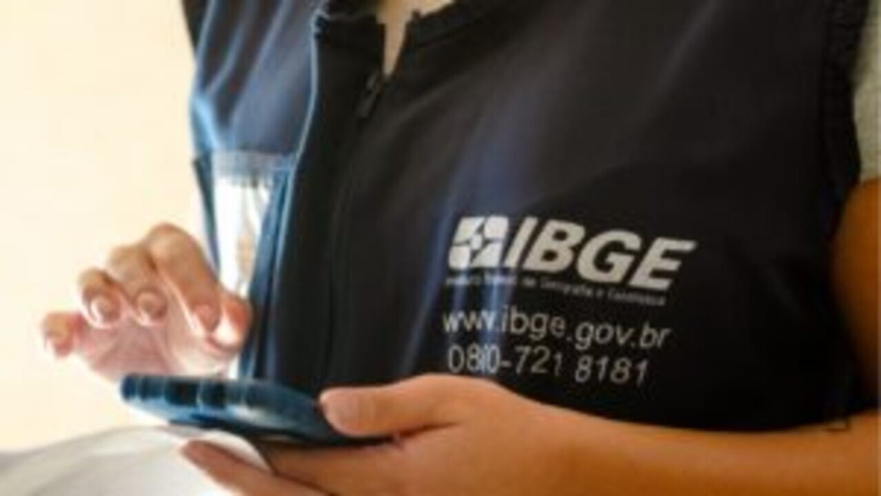 Recenseador com colete do IBGE segurando dispositivo de coleta de informações do Censo