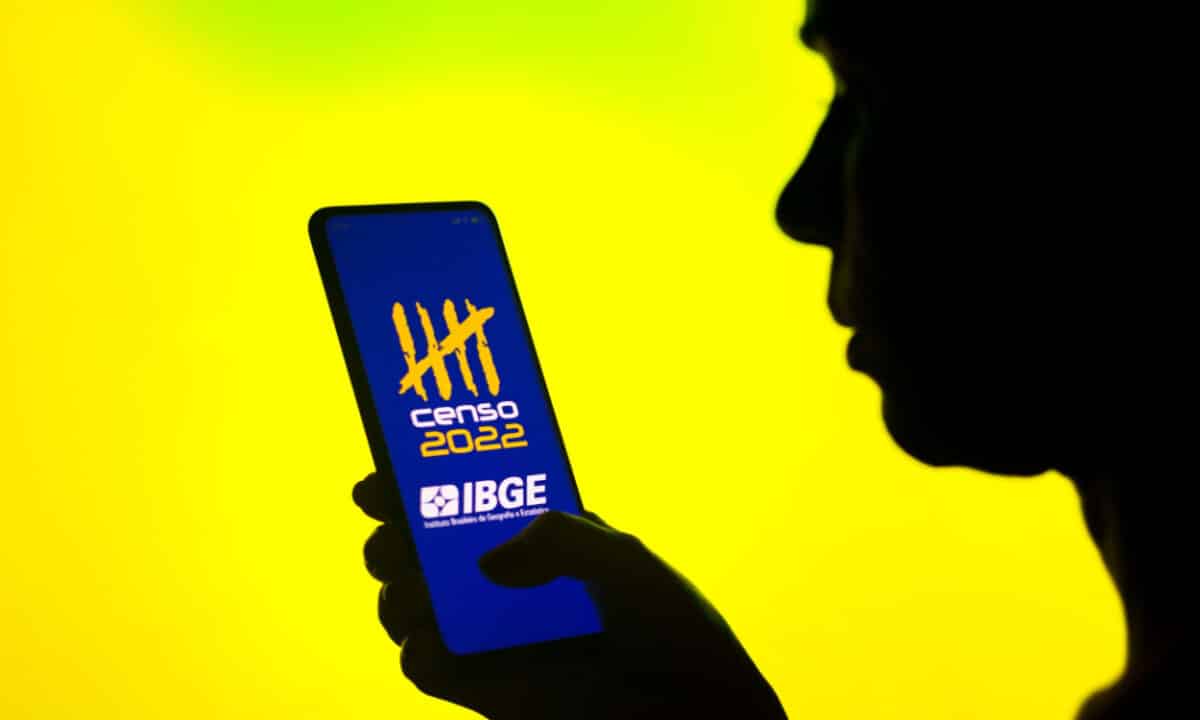 Homem segurando um celular com a logo do Censo do IBGE 2022 na tela