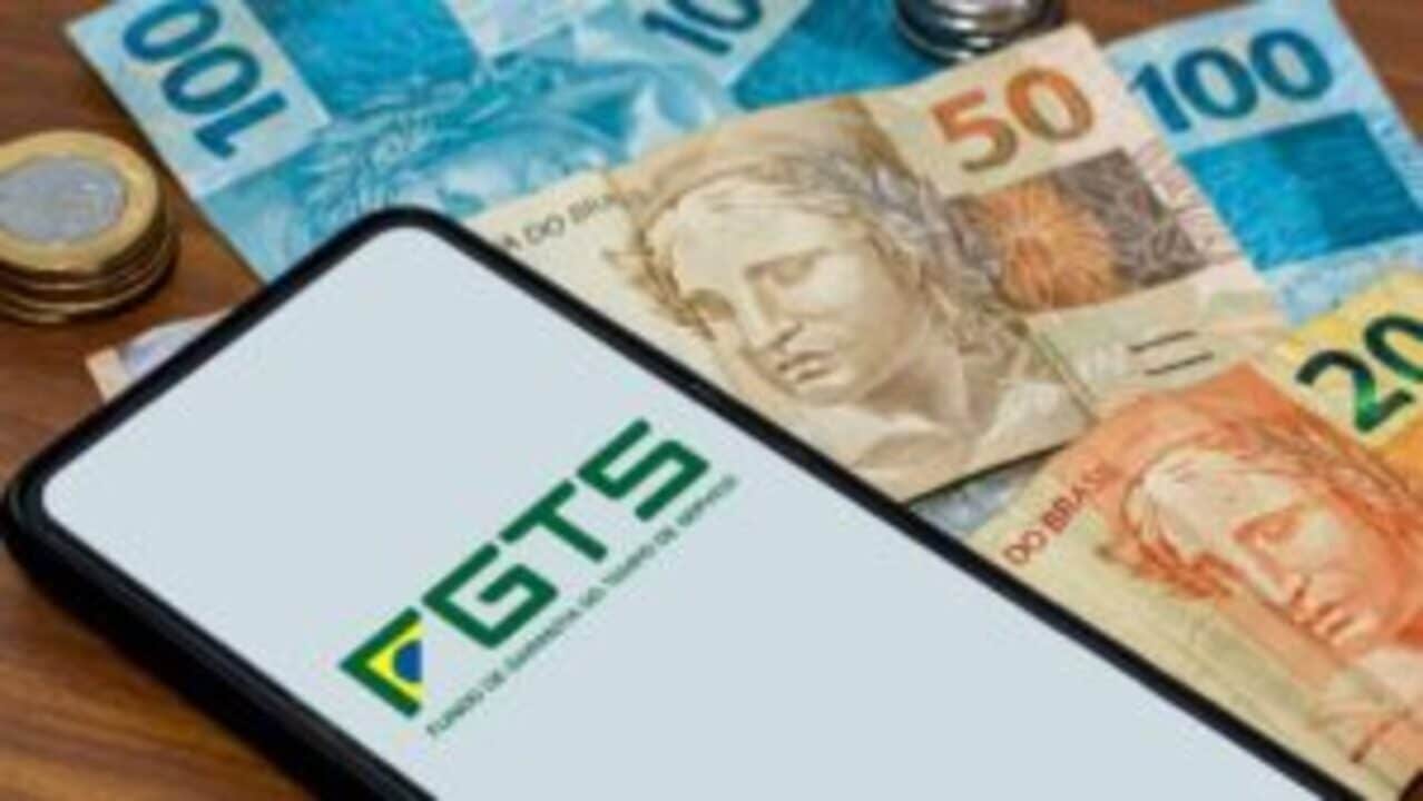 Celular com aplicativo do FGTS ao lado de várias notas de real e moedas