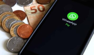 Celular com logo do WhatsApp Pay e moedas e uma nota de cinquenta reais dobrada ao lado