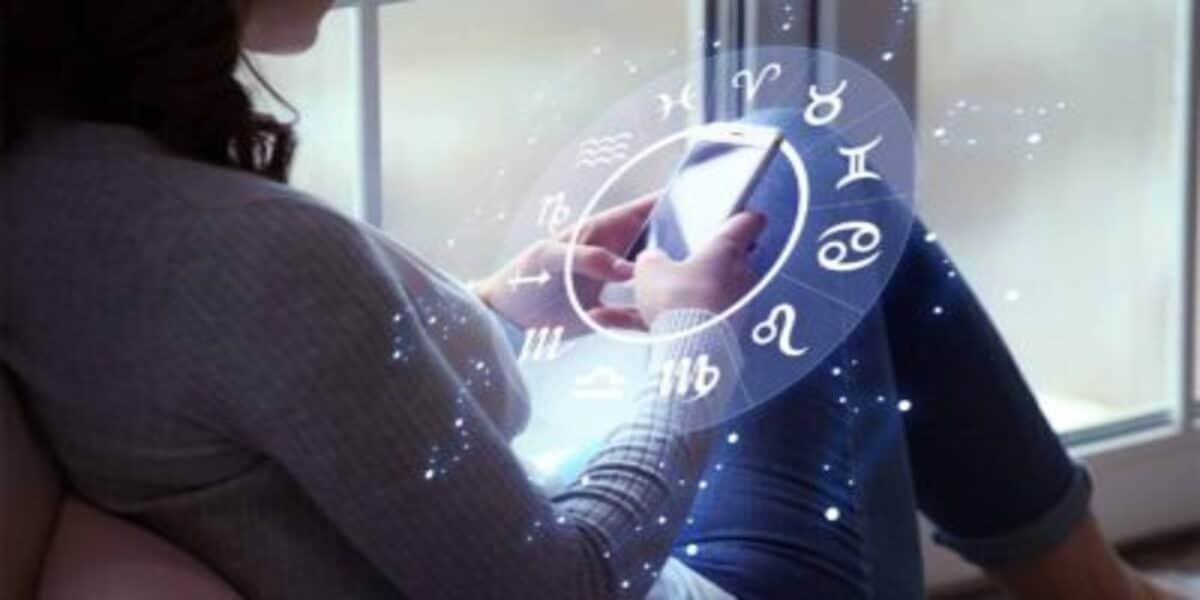 Pessoa mexendo no celular com desenho gráfico dos signos do zodiaco