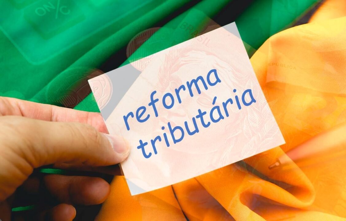 Ao fundo uma bandeira do Brasil e em cima uma mão segurando um papel escrito "reforma tributária"